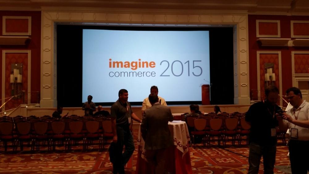 Photo of a conference getting ready to start. On the large screen, the title of the conference "Imagine Commerce 2015"