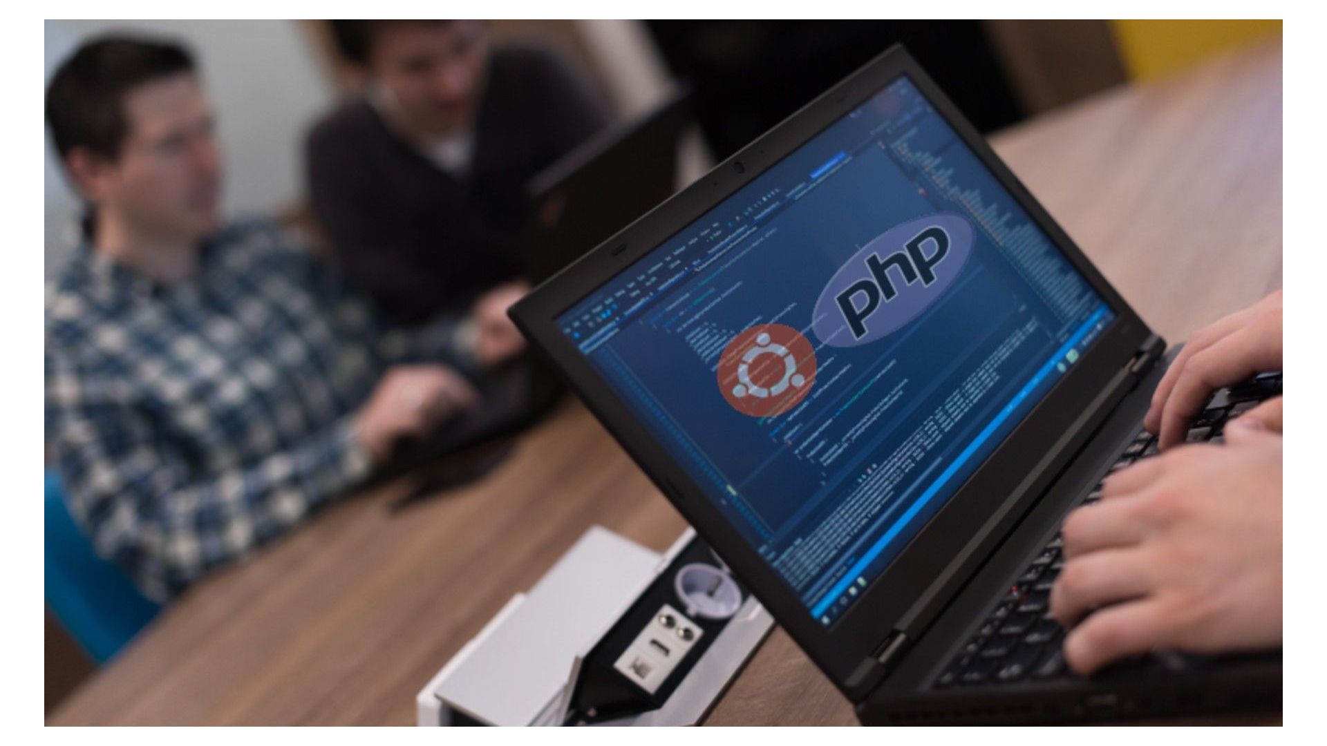 Image of a conference room with people working. A laptop screen is shown with the symbols for Ubuntu and PHP on the screen.